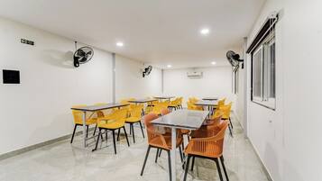 Una sala de conferencias con varias mesas y sillas, ventiladores de techo, un letrero de salida de emergencia y un equipo de aire acondicionado.
