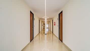 A long, narrow hallway with doors on both sides, a fire extinguisher on the right wall, and a clean, shiny floor.