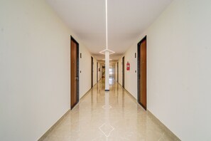 A long, narrow hallway with doors on both sides, a fire extinguisher on the right wall, and a clean, shiny floor.