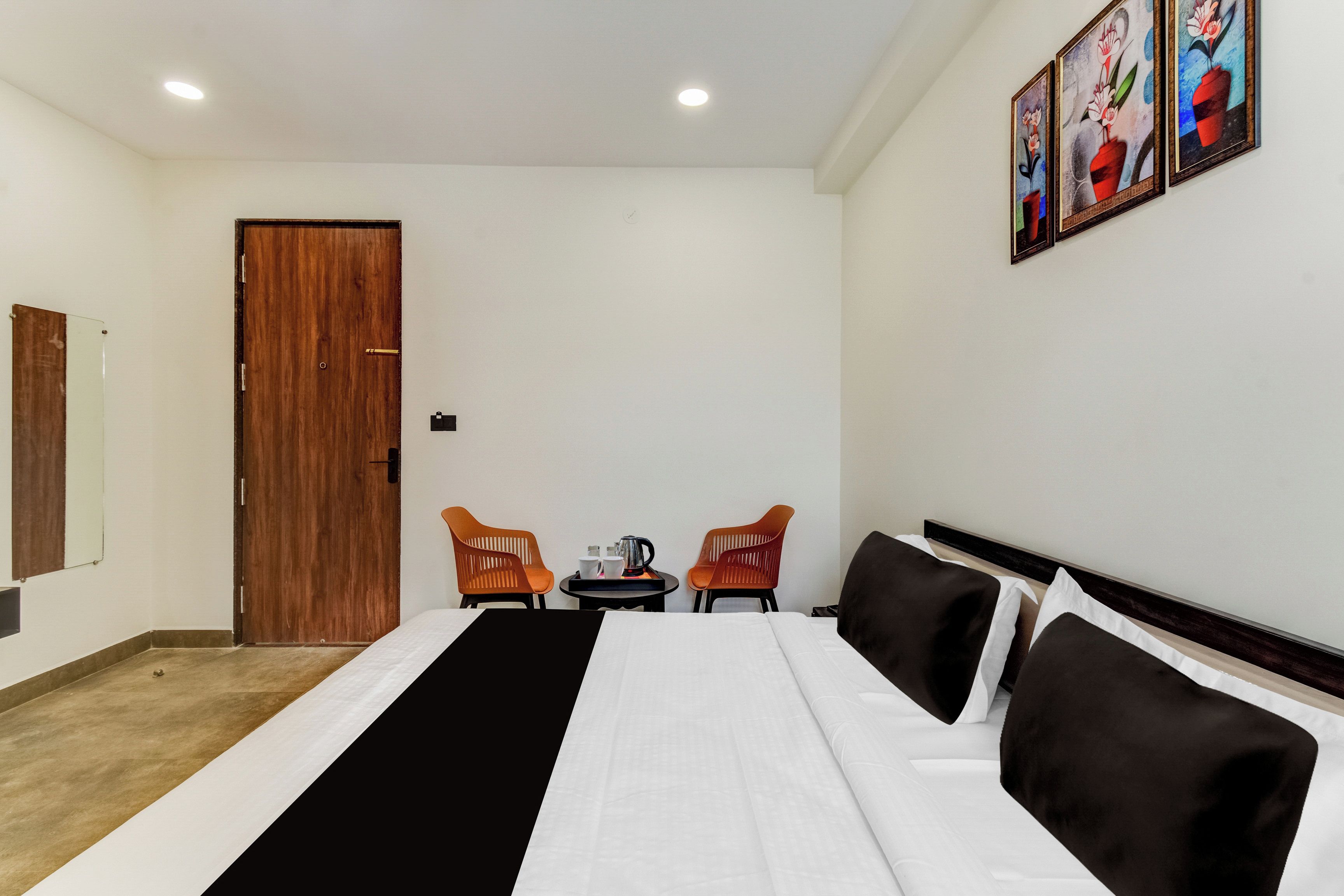 A hotel room with a bed, two chairs, a small table with a kettle, and a door.
