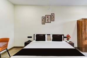 A hotel room with a bed, a nightstand, a chair, and a wooden wardrobe. - Townhouse OAK Owaisi Hospital (Hyderabad)