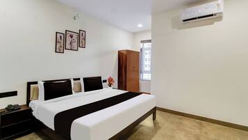 A hotel room with a bed, a nightstand, a phone, a window, and an air conditioning unit.