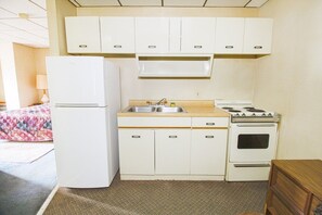 A compact kitchenette with a refrigerator, sink, stove, and cabinets. - King Bed with Kitchenette (Liberal KS)
