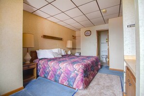 Ein Hotelzimmer mit Bett, Nachttischlampen, einem kleinen Schreibtisch, einem Stuhl, Toilette und Duschbereich.