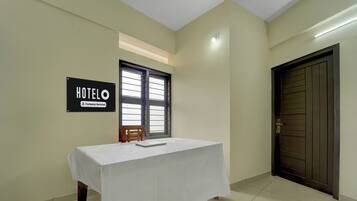 Habitación de hotel con una mesa cubierta de blanco, un letrero que indica que es un hotel con servicios para empresas, una ventana con persianas y una puerta con manija.