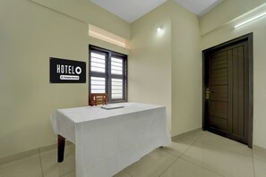 Habitación de hotel con una mesa cubierta de blanco, un letrero que indica que es un hotel con servicios para empresas, una ventana con persianas y una puerta con manija.