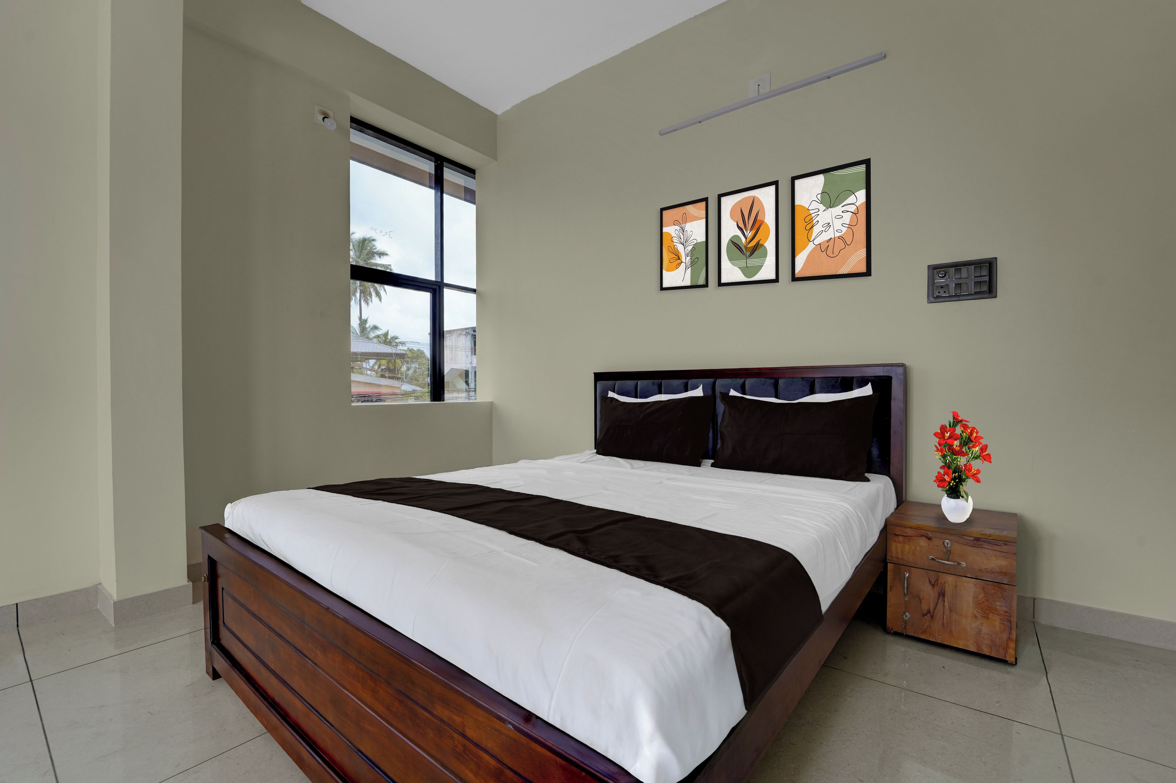 Une chambre à coucher avec un grand lit, une table de chevet, un vase de fleurs et deux œuvres d’art encadrées accrochées au mur.