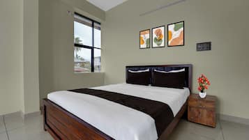 A bedroom with a large bed, a nightstand, a vase with flowers, and two framed artworks on the wall.
