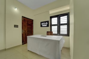 Una habitación de hotel con una puerta de madera, un letrero que indica servicio de empresa, una ventana con persianas y una mesa con una computadora portátil.