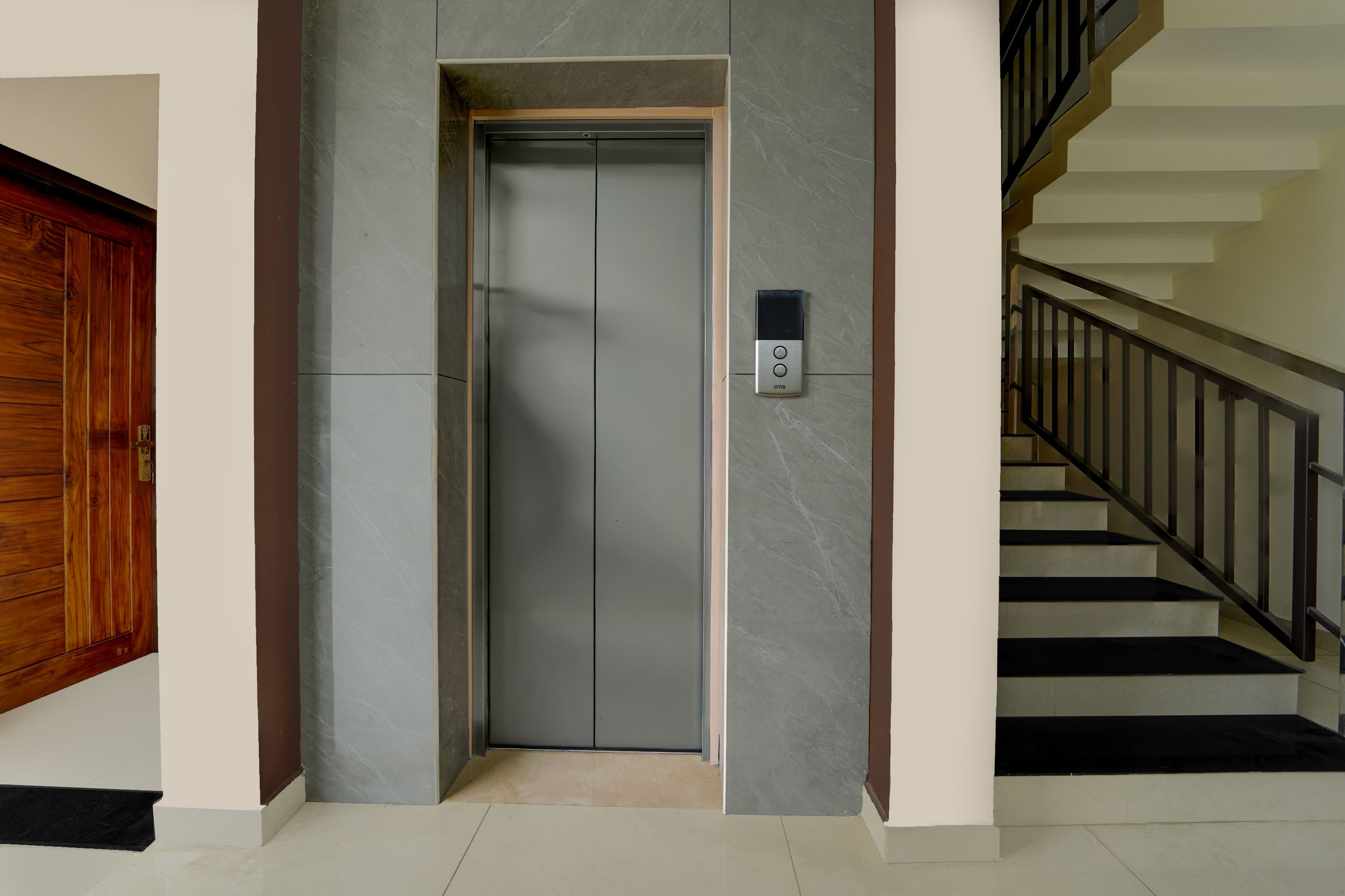 Un ascenseur moderne doté d’un panneau de commande, d’une porte en bois et d’un escalier avec des rampes noires.