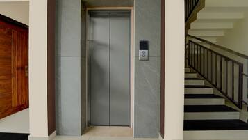 A modern elevator with a control panel, a wooden door, and a staircase with black railings.