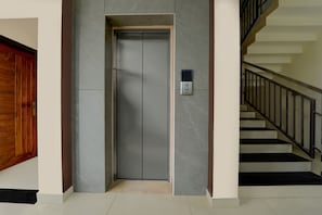 Un ascensor moderno con un panel de control, una puerta de madera y una escalera con barandillas negras.