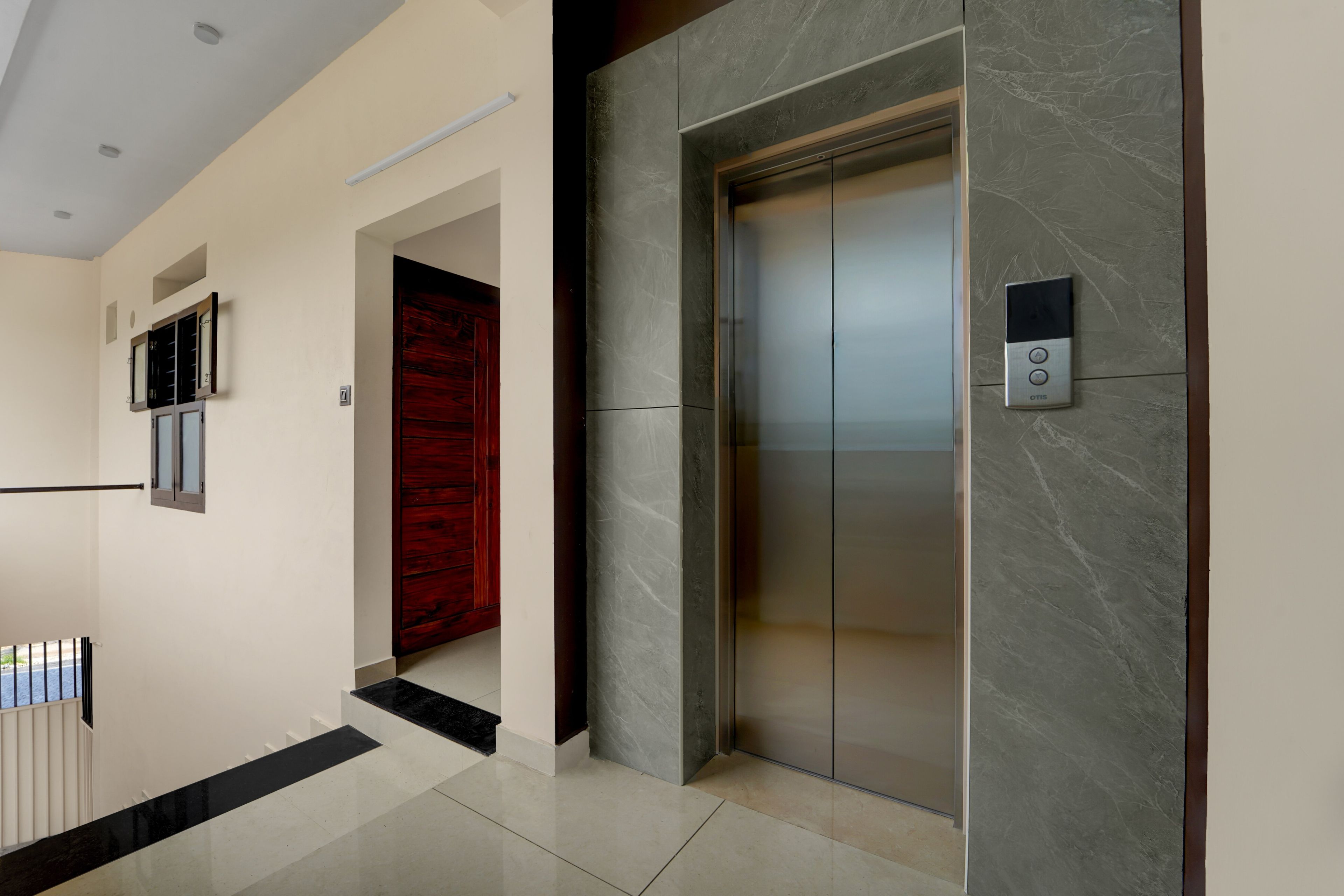 Un elevador moderno con un tablero de control, una puerta roja y una pared de mármol.