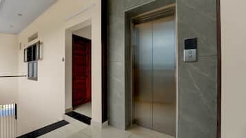 Un elevador moderno con un tablero de control, una puerta roja y una pared de mármol.