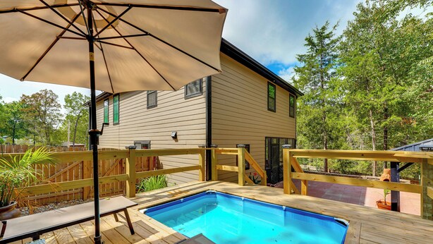Ein Garten mit Swimmingpool, Holzterrasse und einem Haus.