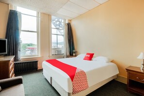 Ein Hotelzimmer mit Bett, Schreibtisch, Stuhl, Fernseher und einem Fenster mit Vorhängen.