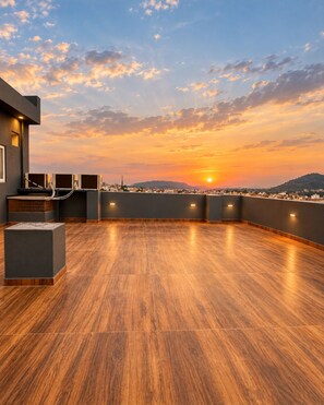Una terrazza sul tetto con pavimento in legno, un'area salotto e vista sulla città al tramonto.