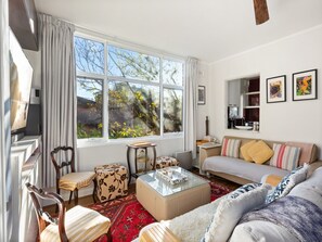 A well-lit living room with a sofa, chairs, a coffee table, and a large window offering a view of trees and a building. - Peaceful Hideaway 2-bed Apartment Mosman (Sydney)