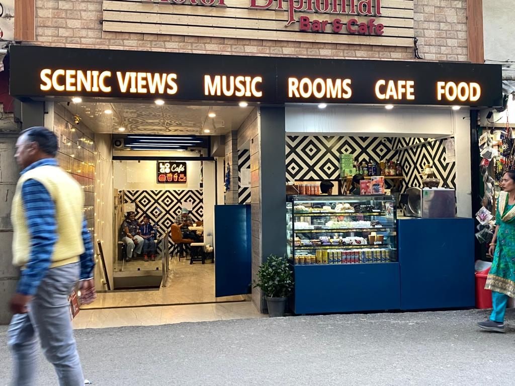 Bar y cafetería con un cartel que enumera servicios como vistas panorámicas, música, habitaciones, cafetería y comida.
