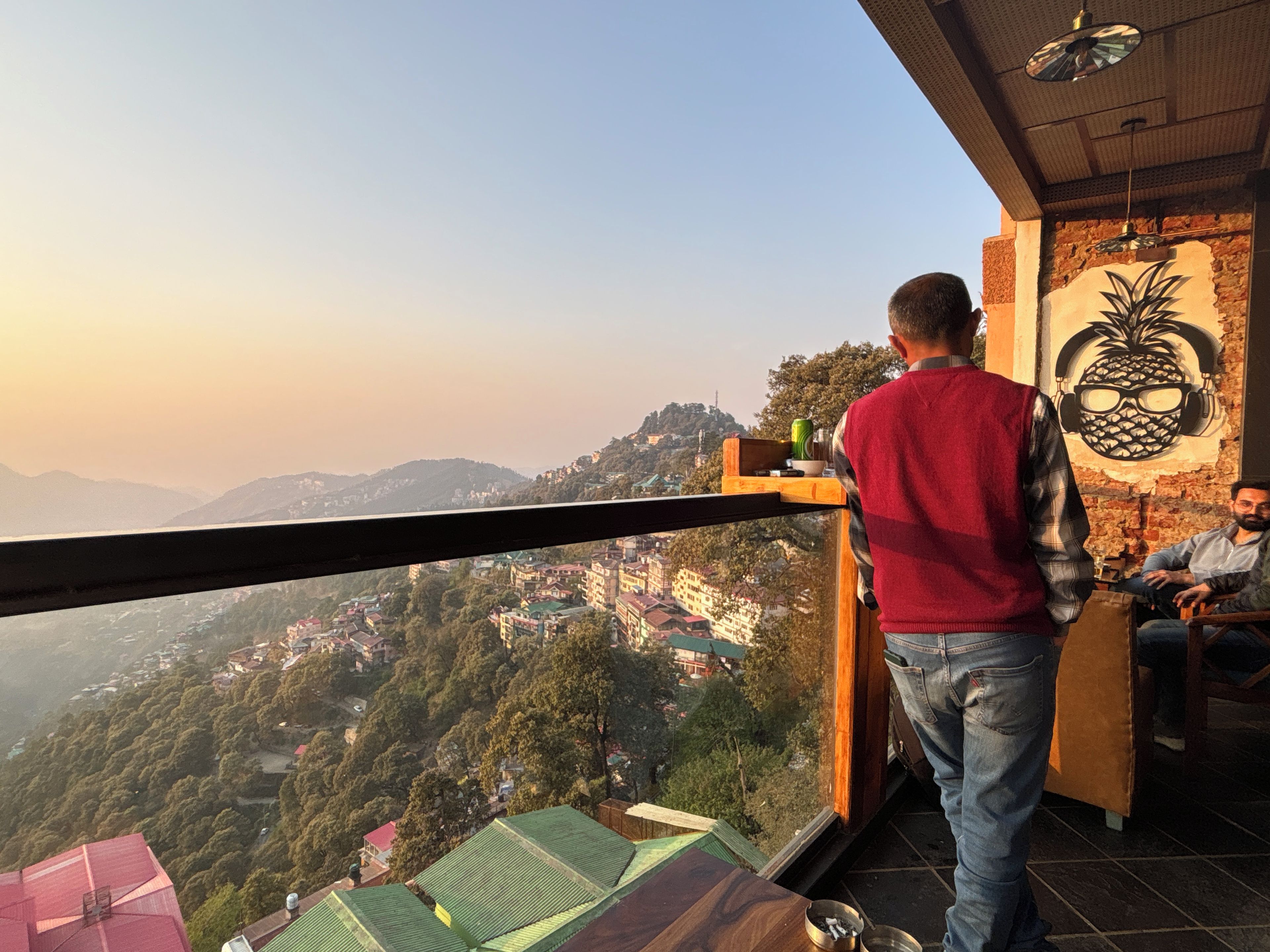 Un balcón con vistas a un paisaje montañoso, un mural de piña y una persona sentada en el interior.