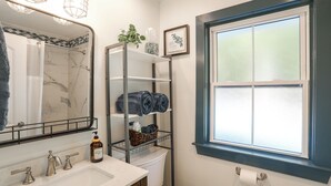 Et badeværelse med et hvidt håndvask, et spejl, en bruser, et toilet og et vindue med matteret glas.