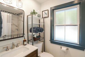 Une salle de bain avec un lavabo blanc, un miroir, une douche, des toilettes et une fenêtre en verre dépoli.