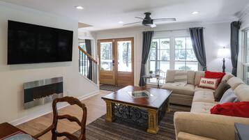 A living room with a flat-screen TV, a fireplace, a sofa, a coffee table, and a ceiling fan.