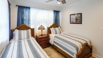 Quarto de hotel com duas camas de solteiro, um ventilador de teto, mesa de cabeceira com abajur e um quadro na parede.