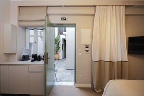 Ett hotellrum med en säng, ett skrivbord med en telefon och en kaffebryggare, en tv som är monterad på väggen och en dörr som leder ut till en korridor.