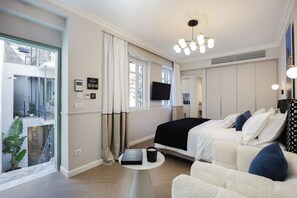 Et hotelværelse med seng, sofa, lille bord, fjernsyn og en balkon med planter.