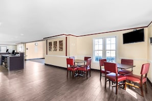 A hotel lobby with a reception desk, a dining area with red chairs and tables, and a large window providing natural light. - King Bed Non Smoking (Tulsa)