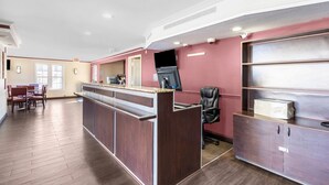 Uma área de recepção com balcão, espaço de estar com cadeiras e mesa com computador.