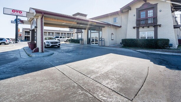 Hotel com estacionamento coberto, placa indicando OYO Inn & Suites e céu limpo.