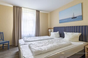 Ein Hotelzimmer mit einem Bett, einem Sessel, einem Gemälde mit einem Segelboot und einem Fenster mit Vorhängen.