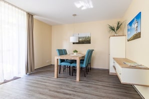 Ein Zimmer mit einem Holztisch, zwei Stühlen, einer weißen Kommode und einem Gemälde eines Leuchtturms.