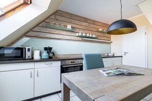 A kitchen with a wooden ceiling, a dining table with a magazine, and a hanging light fixture. - Sielwärts - Spiekeroog (Carolinensiel)