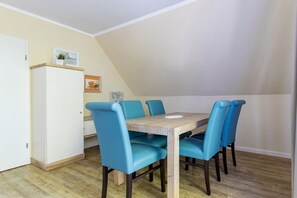 A dining area with a wooden table and four blue chairs, a white cabinet, and a white door. - Sielwärts - Spiekeroog (Carolinensiel)