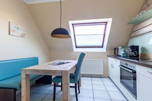 A compact kitchen with a dining table, chairs, a window, and a built-in oven. - Sielwärts - Spiekeroog (Carolinensiel)
