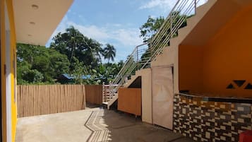 Ein offener Wohnbereich mit einer Treppe, die zu einer erhöhten Ebene führt, einer gefliesten Wand und einem roten Plastikstuhl.