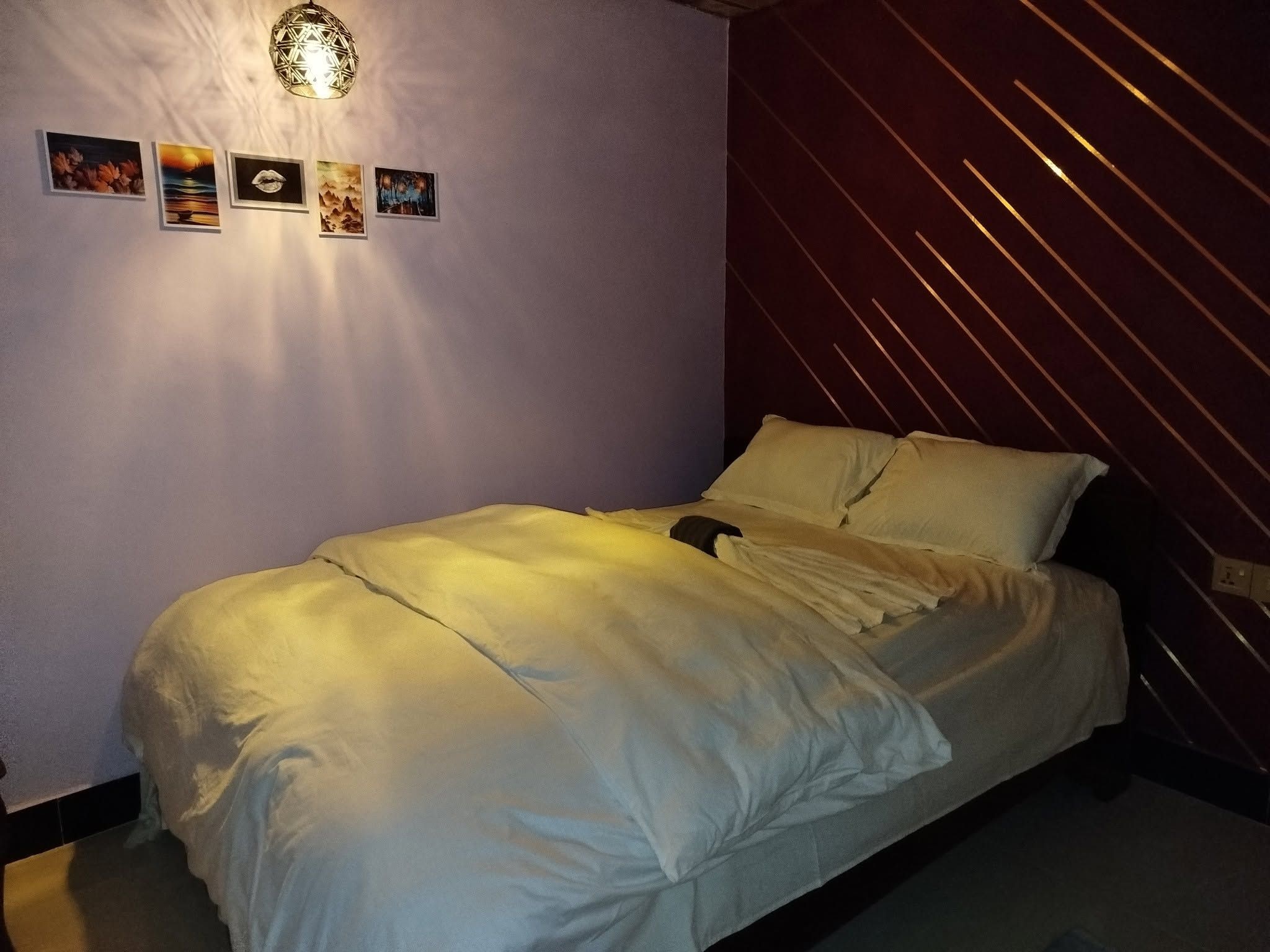 Une chambre à coucher avec un lit, un luminaire fixé au mur et quatre tableaux encadrés.