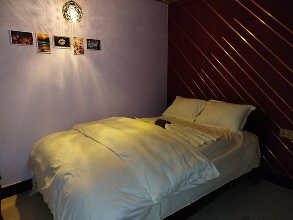 A bedroom with a bed, a wall-mounted light fixture, and four framed pictures.