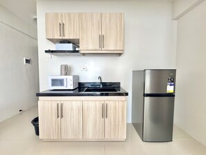 Eine kompakte Küche mit hellen Holzschränken, einem Edelstahlkühlschrank, einer Mikrowelle und einer schwarzen Arbeitsplatte.