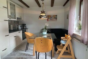 A modern kitchen with white cabinets, a glass dining table, and wooden chairs. - by the lake with views of the lake and the Bavarian Forest, ground floor (Arrach\/ Kummersdorf)