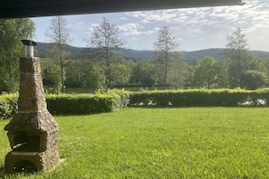 A stone-built outdoor oven in a grassy area with a view of a forested landscape and hills in the background. - by the lake with views of the lake and the Bavarian Forest, ground floor (Arrach\/ Kummersdorf)