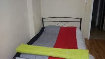 A single bed with a metal frame, grey and red bedding, and a yellow blanket.