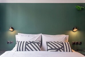 A bed with white bedding and black and white striped pillows, two wall-mounted light fixtures, and a green wall.