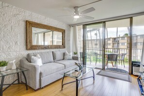 Ein modernes Wohnzimmer mit einem grauen Sofa, einem Glastisch und einem Deckenventilator.