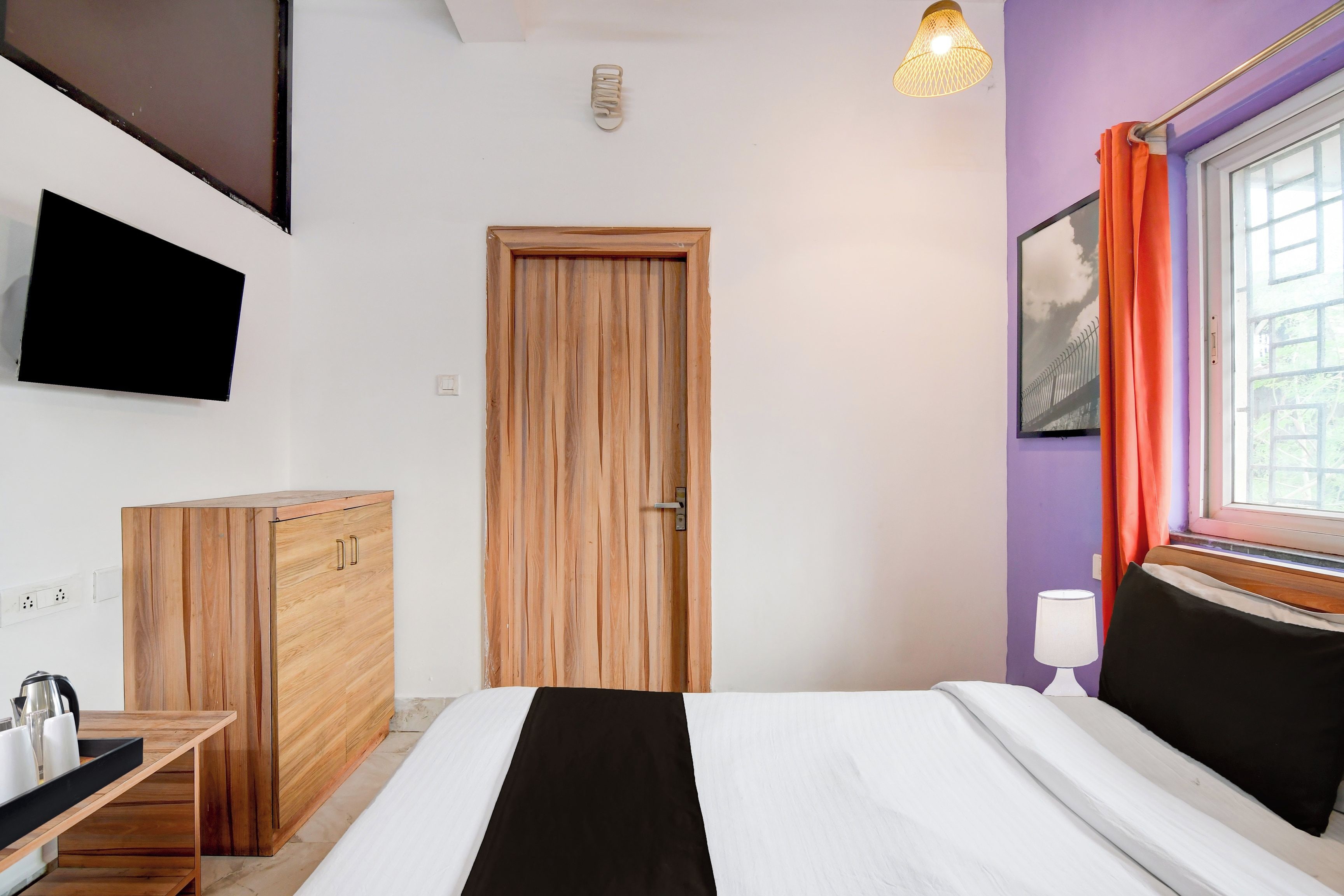 Ein Schlafzimmer mit einem Bett, einem Holzschrank, einem an der Wand befestigten Fernseher und einem Fenster mit Vorhängen.