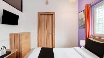Ein Schlafzimmer mit einem Bett, einem Holzschrank, einem an der Wand befestigten Fernseher und einem Fenster mit Vorhängen.