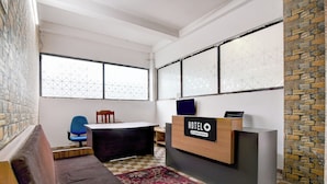 Zona de recepción de un hotel con un mostrador, una silla azul, un banco de madera y una alfombra estampada.